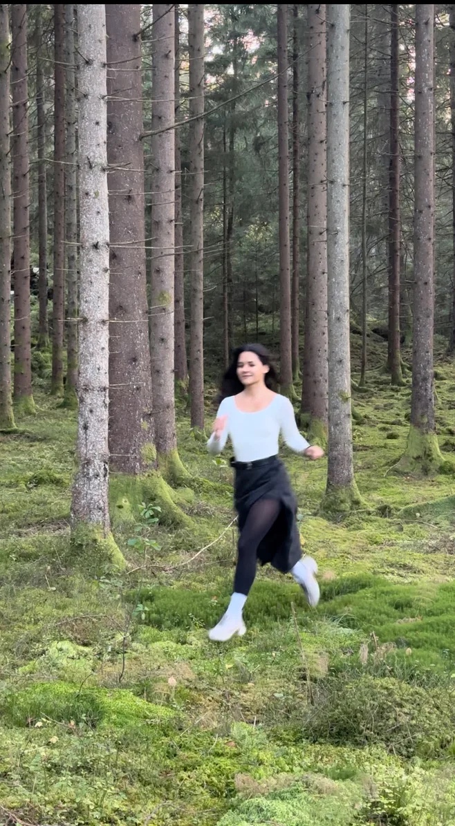 Mariana running through a pine forest towards the camera, smiling